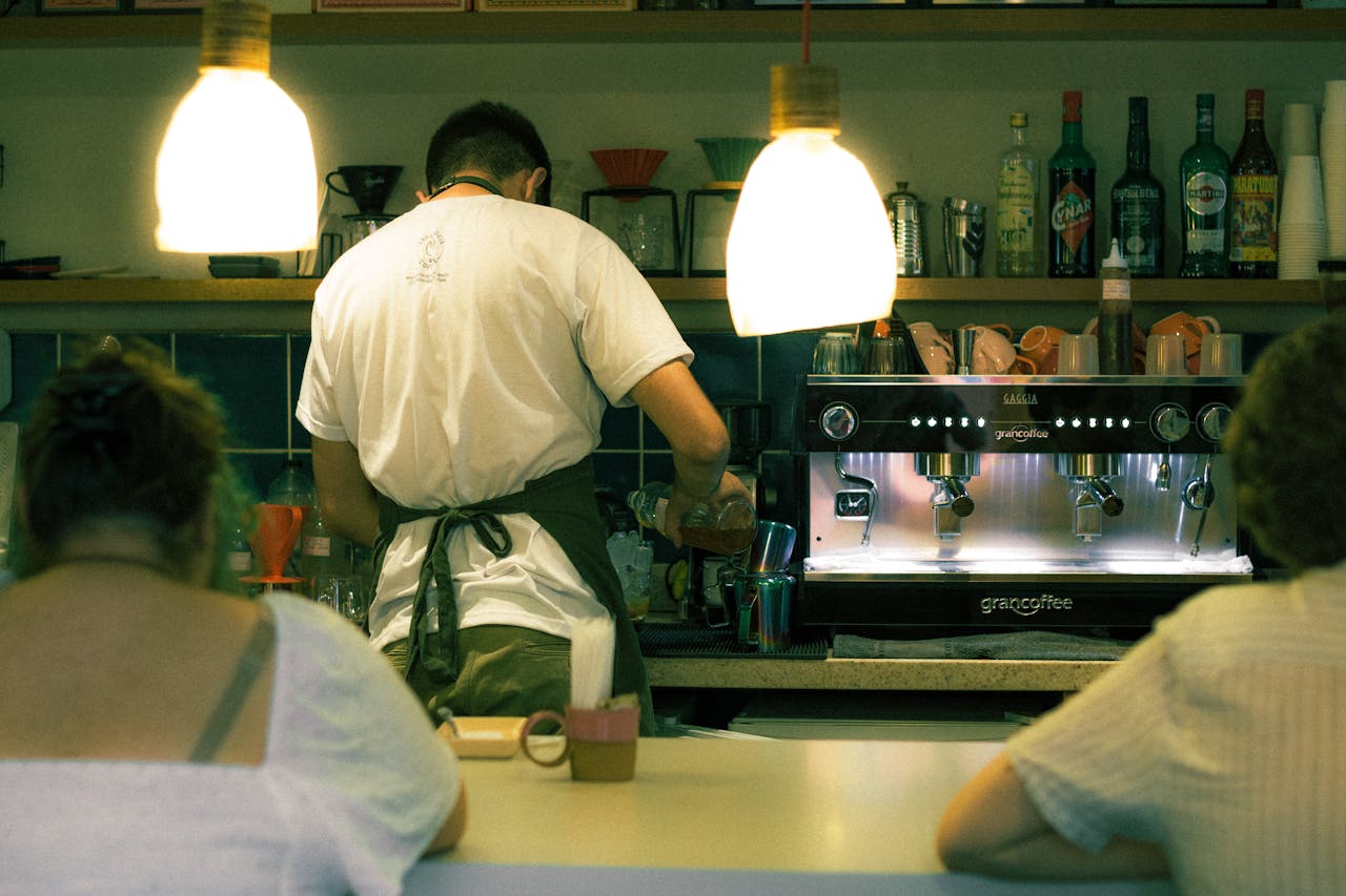 A barista skillfully prepares coffee at the espresso machine in a warmly lit café environment.