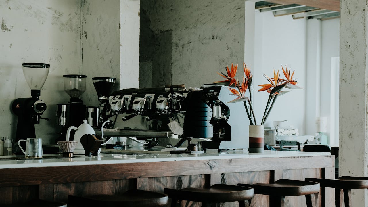 Stylish café interior featuring espresso machine, grinders, and floral decor on a sleek counter.