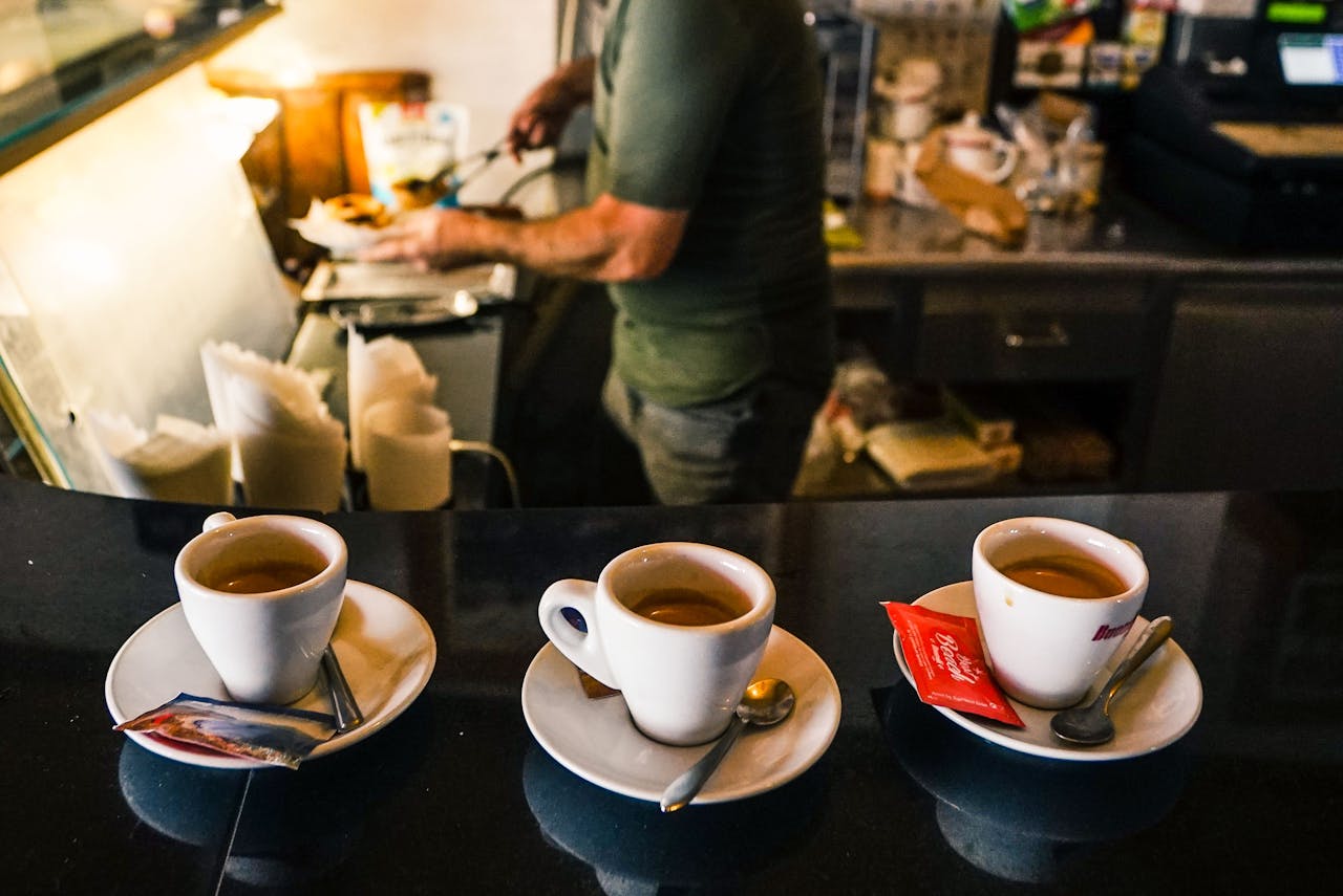 A barista in a café preparing espresso drinks on a countertop with three coffee cups in focus.